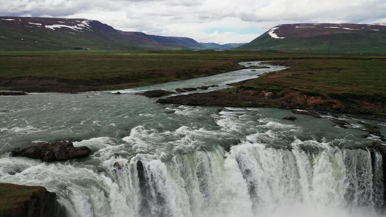 hombre parado frente a la cascada de godafoss con aguas torrenciales que fluyen del río en el norte de islandia - disparo de drones