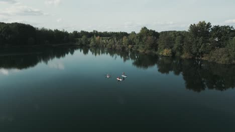 drone over beautiful dark lake in germany flies over sup stand-up paddlers while camera is panning down on them