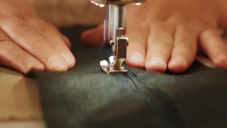 hand of the seamstress is using white industrial sewing machine sew zipper (slide fastener) of crotch black pants close-up.