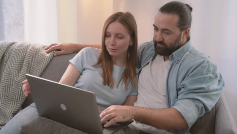 a happy couple have a relaxed conversation sitting on the sofa and looking at the laptop