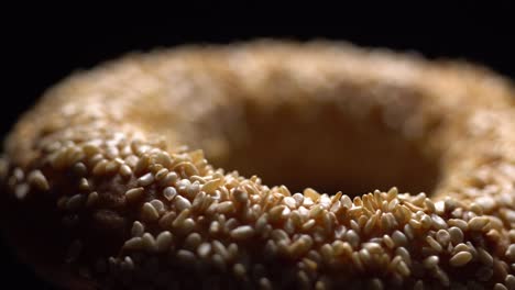 fresh bagels with sesame seeds in rotation. black background. extreme closeup.