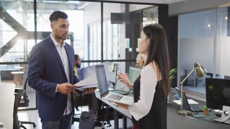 Two-diverse-businesspeople-discussing-together-using-laptop-and-standing-at-table