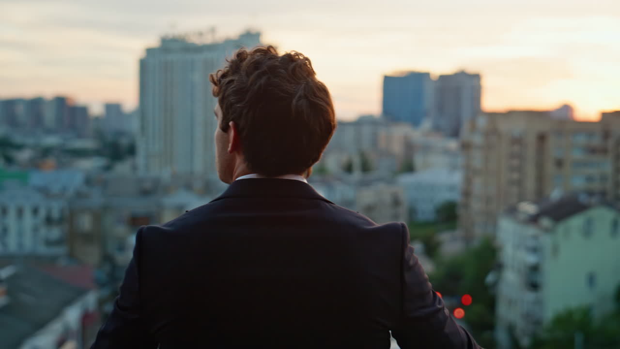 Back view businessman standing balcony overlooking city dusk. Confident man