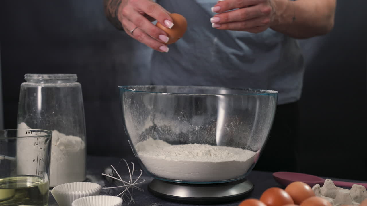Close up of cracking eggs into a bowl during the cupcake preparation process, tracking follows hands to open shell and drop yolk