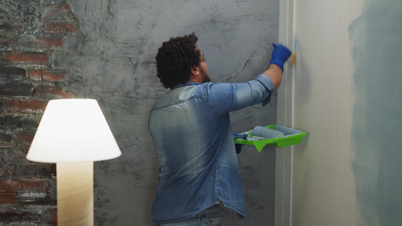 joven pintor negro en ropa de mezclilla pinta la esquina de la habitación