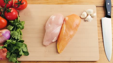 raw chicken breast with vegetables on a cutting board