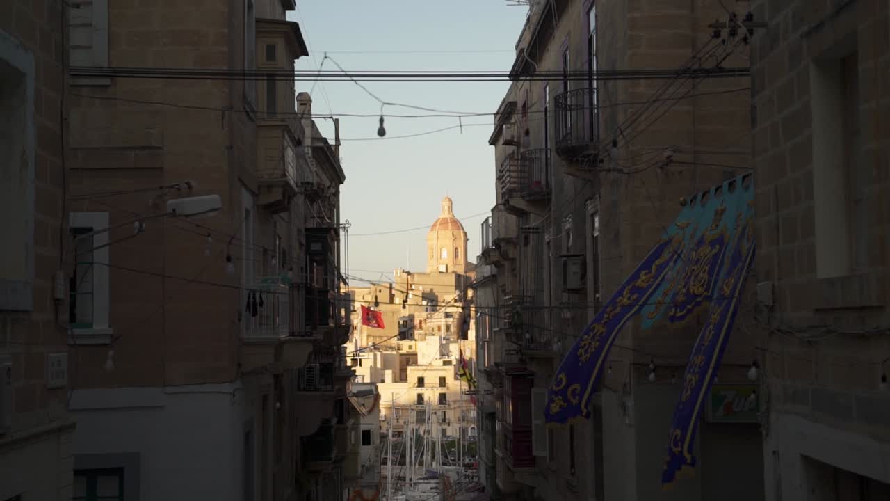 Strada stretta con bandiere a Malta, con vista su una delle tre città