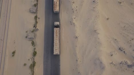 Volar-Hacia-Atrás-Sobre-Una-Larga-Fila-De-Camiones-En-El-Desierto-Sobre-Un-Camino-Agrietado