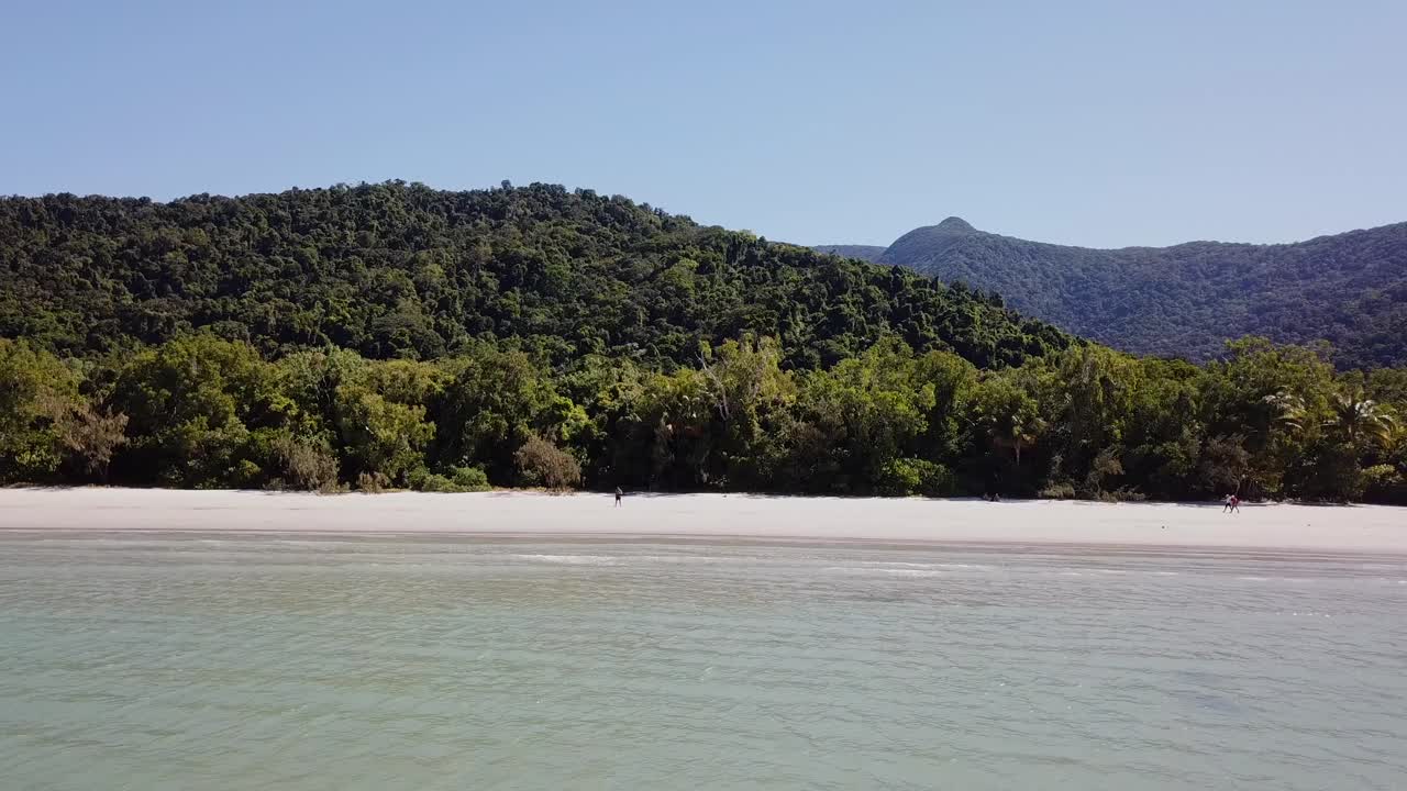 Aerial: Drone moving away from a lone figure standing on a white sandy beach to slowly reveal more of the stunning landscape, in Cape Tribulation, Far North Queensland