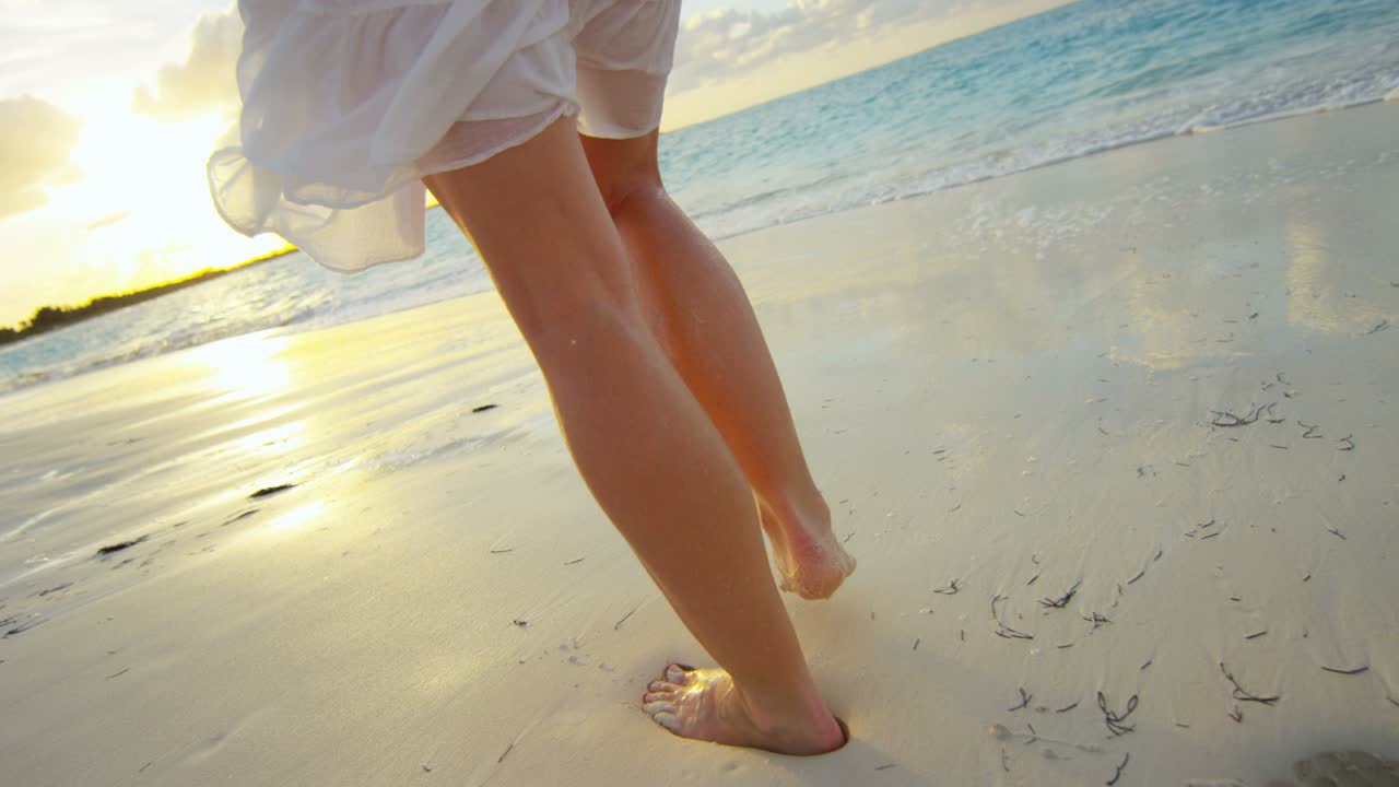 Gambe femminili caucasiche a piedi nudi sulla spiaggia al tramonto