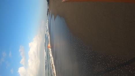 person carrying surfboard and walking on sandy beach in bali, pov vertical view