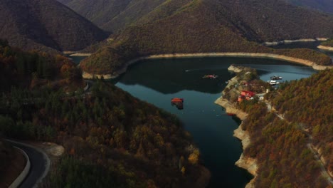 Flying-over-Vucha-dam-during-a-colorful-autumn-with-moving-boat-in-the-water