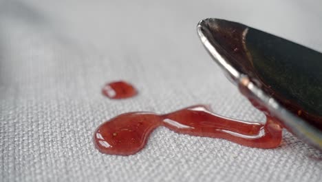 close-up of a spoon dripping jam onto a white tablecloth