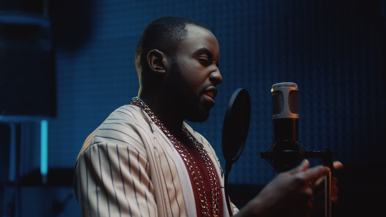 마이크에서 랩 노래를 읽고 어두운 사운드 스튜디오에서 녹음하는 젊은 잘생긴 남자 랩퍼를 닫습니다.