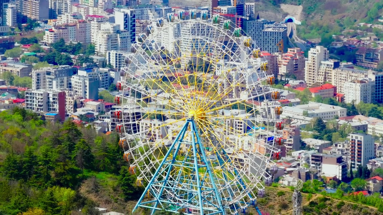 Vista aérea de drone de Tbilisi do Monte Mtatsminda, apresentando roda-gigante, horizonte da cidade, rio e vastas paisagens urbanas.