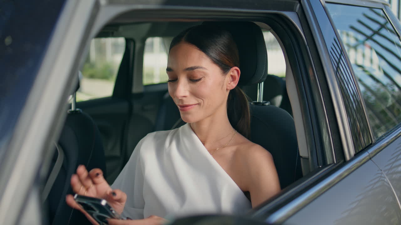 una mujer de negocios feliz sentada en un automóvil mirando un teléfono inteligente enviando mensajes de texto de cerca.