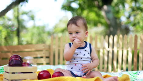 lovely child in light summer clothes sitting in the garden. kid holding thumb in mouth looking ahead not noticing flying soap bubbles.