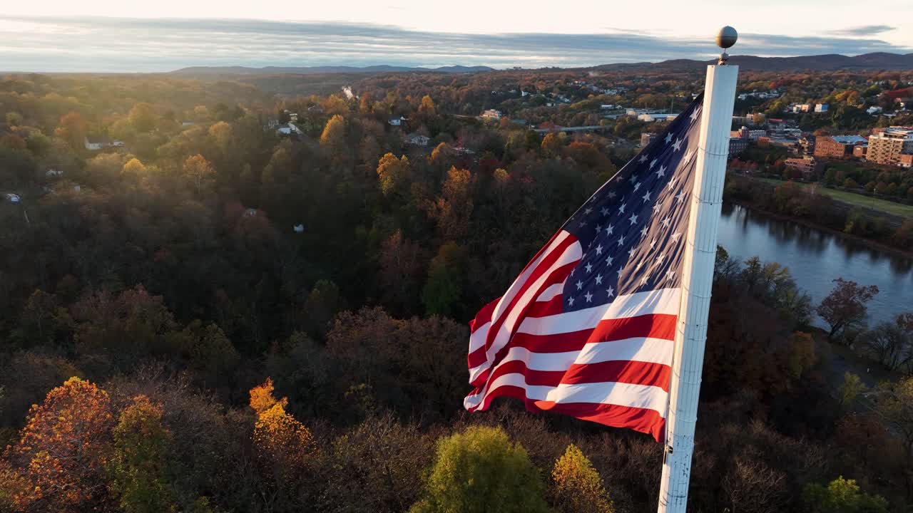 Ripresa aerea cinematografica della bandiera americana che sventola nella brezza durante l'ora d'oro dell'alba autunnale