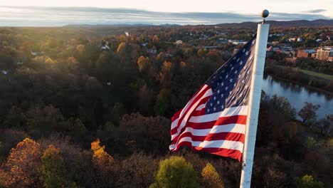 cinematic aerial of american flag waving in breeze during autumn golden hour sunrise light