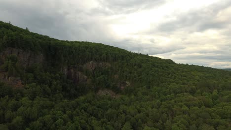 Seitwärts-Aufsteigende-Drohnenaufnahme-Eines-Berghangs-Mit-Felsigen-Wänden-Und-Wolken