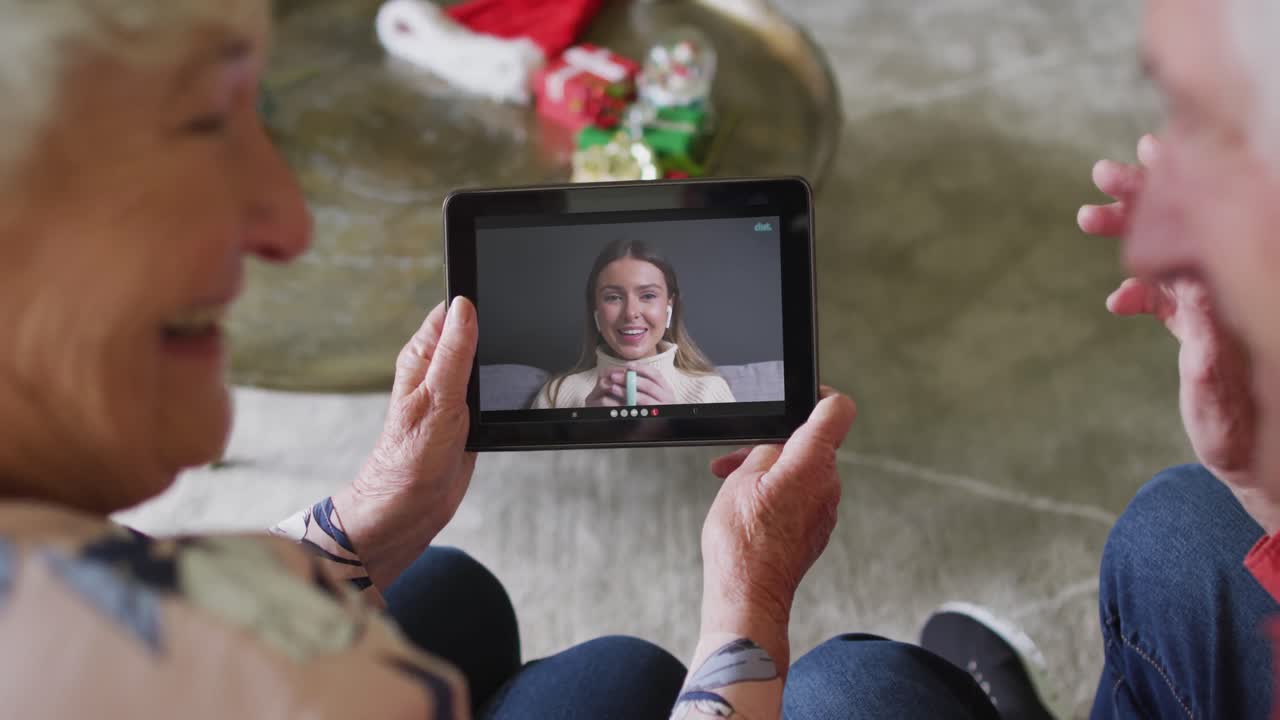 pareja caucásica mayor usando una tableta para una videollamada de navidad con una mujer feliz en la pantalla