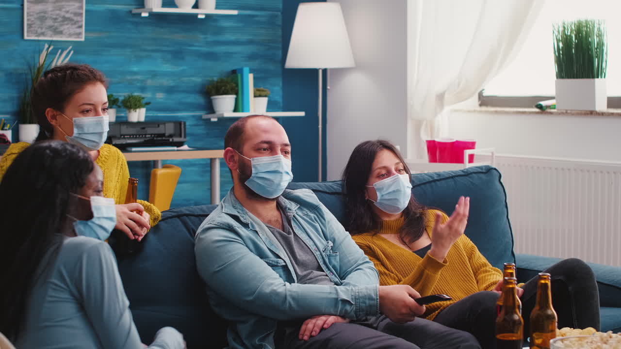 Mixed races of friends looking at tv, man holding remote control
