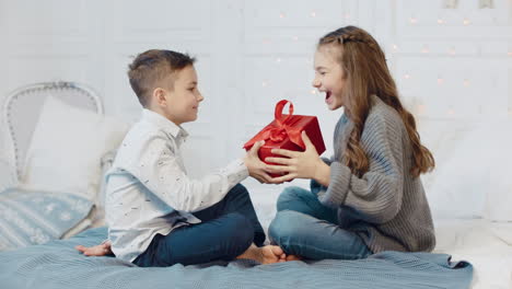 Cheerful-boy-presenting-gift-to-girl-in-living-room.-Happy-girl-closing-eyes