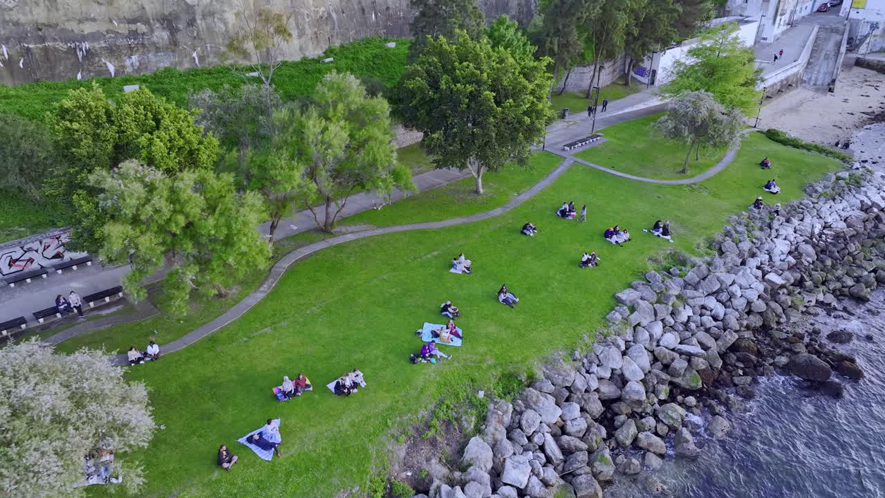 Drone shot of people on the lawn at the park by the river side