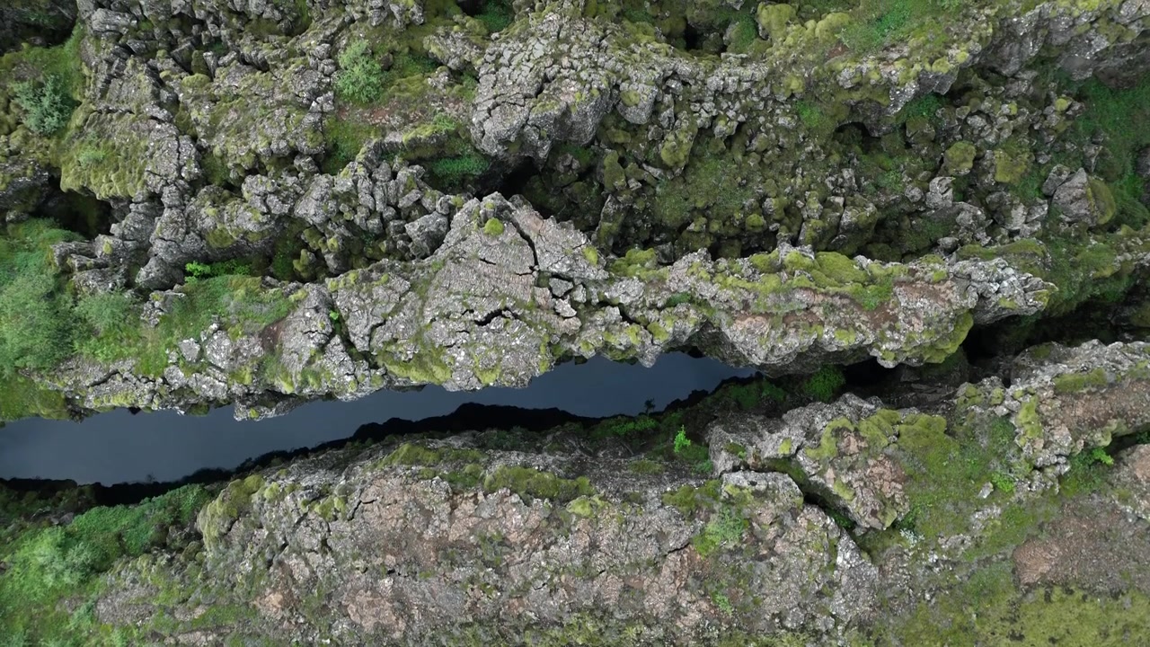 Cảnh quay trên không chi tiết về một khe nứt kiến tạo ở Vườn quốc gia Thingvellir, Iceland, với các khối đá, rêu xanh và nước trong vắt
