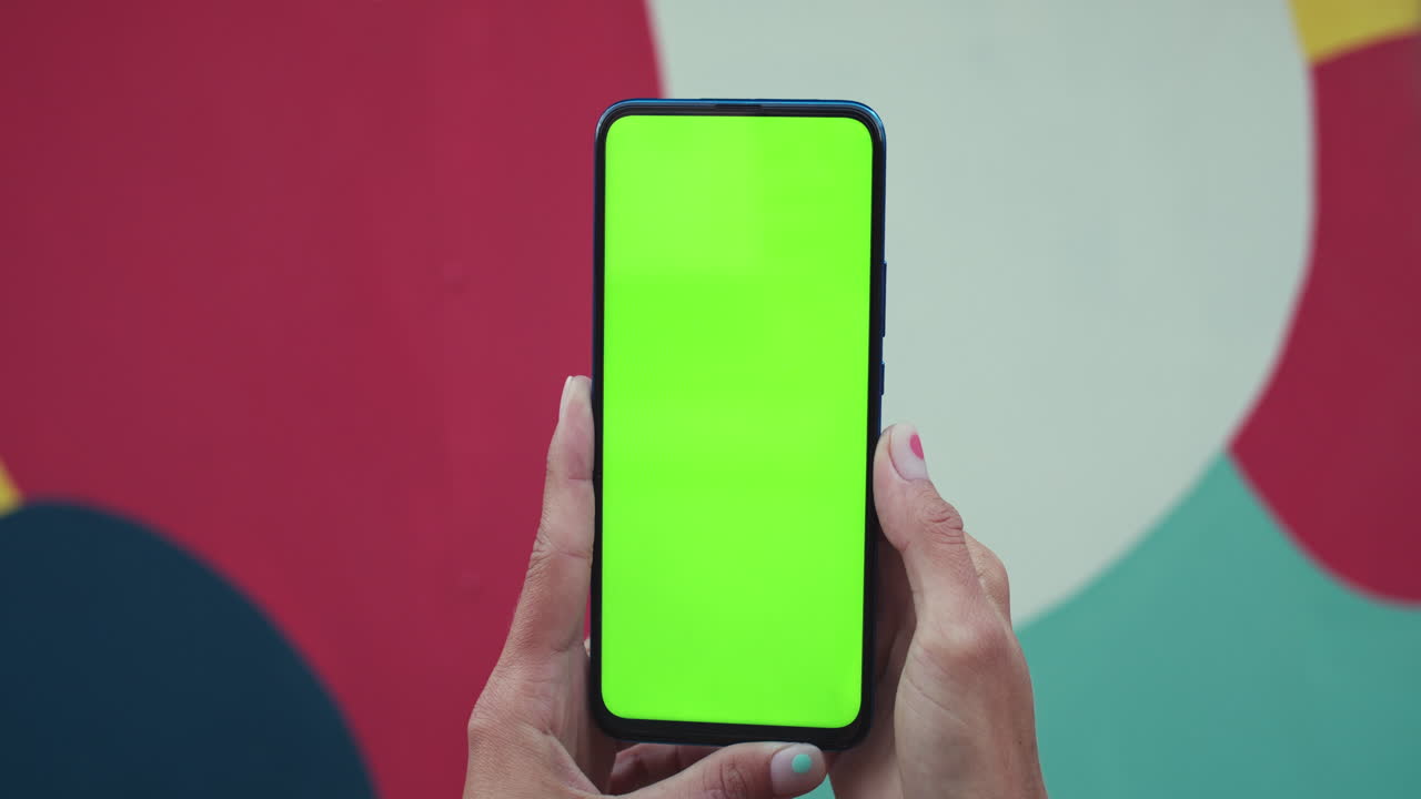 Hands holding a smartphone with a green screen against a colorful background