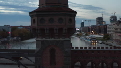 Medium-Shot-of-Oberbaum-Bridge-Tower-in-Berlin,-Germany-rising-up-revealing-Cityscape-Skyline-with-TV-Tower-and-Spree-River,-Aerial-Drone-View