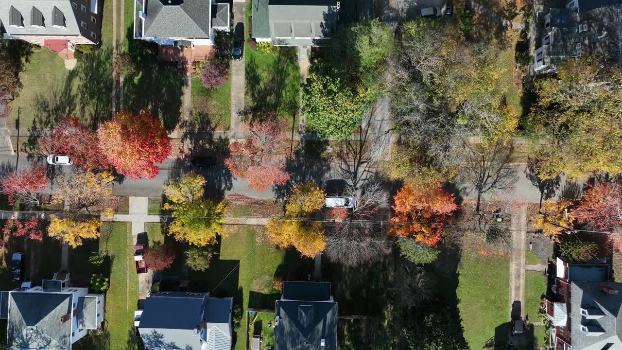 American singles family houses in colonial and craftsman design during sunny day with orange colored trees in fall. Aerial top down rising shot. Street with cars in suburb
