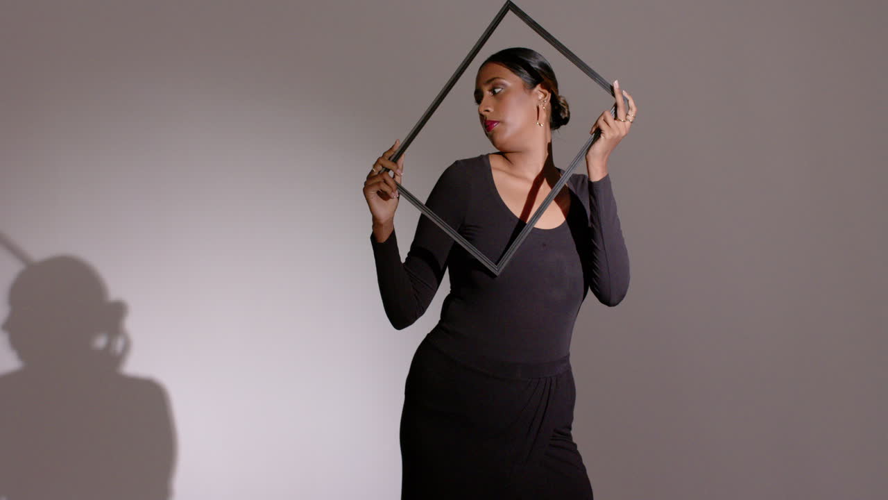 Light revealing Indian woman stepping into studio, adjusting black square frame, copy space