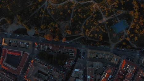 Aerial-birds-eye-overhead-top-down-panning-view-buildings-in-urban-neighbourhood-and-public-park-at-sunset.