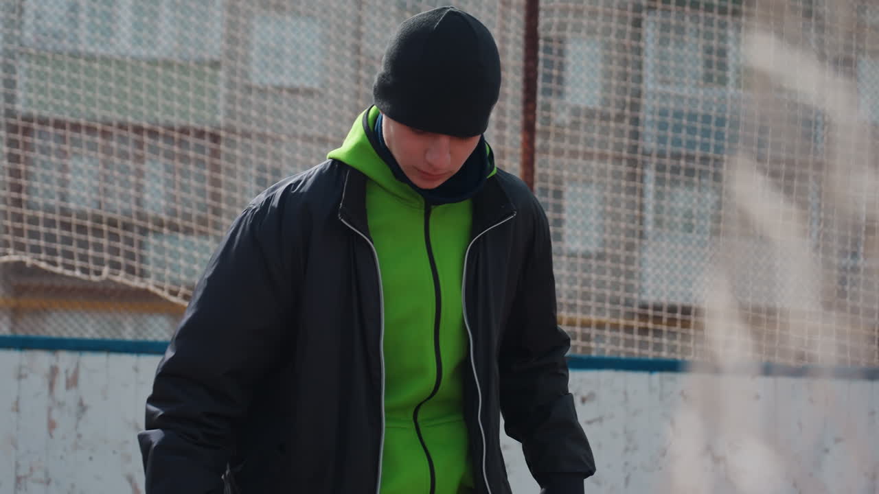 선수가 야외에서 공으로 연습하고, 어린 운동선수가 길거리 축구 훈련에서 실력을 뽐내며, 젊은 스포츠 애호가가 초록색 후드 재킷을 입고 마른 경기장에서 캐주얼한 길거리 축구 실력을 보여줍니다.