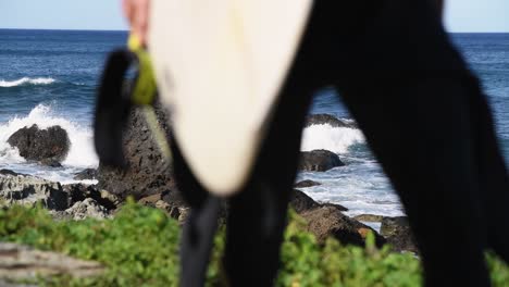 An-unrecognizable-surfer-passes-into-the-ocean-water-with-his-board