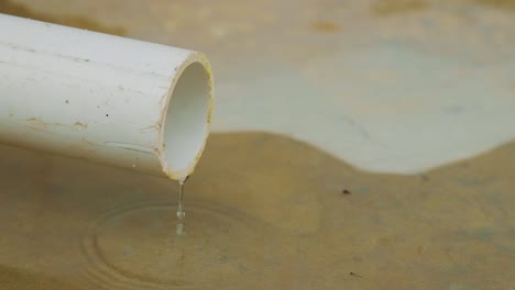 water slowly dripping on a concrete floor from a white pvc pipe making a puddle - close up