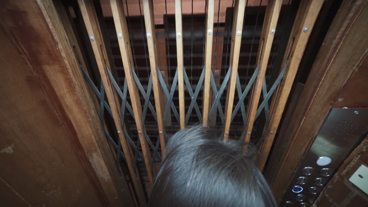 골동품 엘리베이터가 내려갈 때 나무와 철문을 통해 내다보는 사람