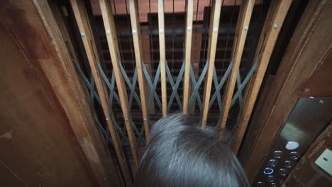 a person looking out through the wood and steel gate of an antique elevator as it lowers