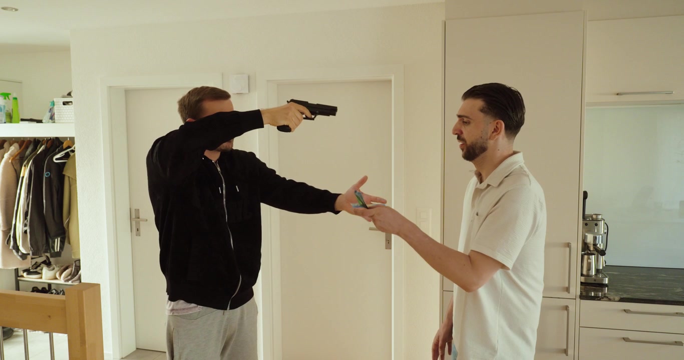 An armed robber points a handgun at a homeowner while demanding money during a home invasion. Concept of armed robbery, extortion, violent crime, and personal safety.
