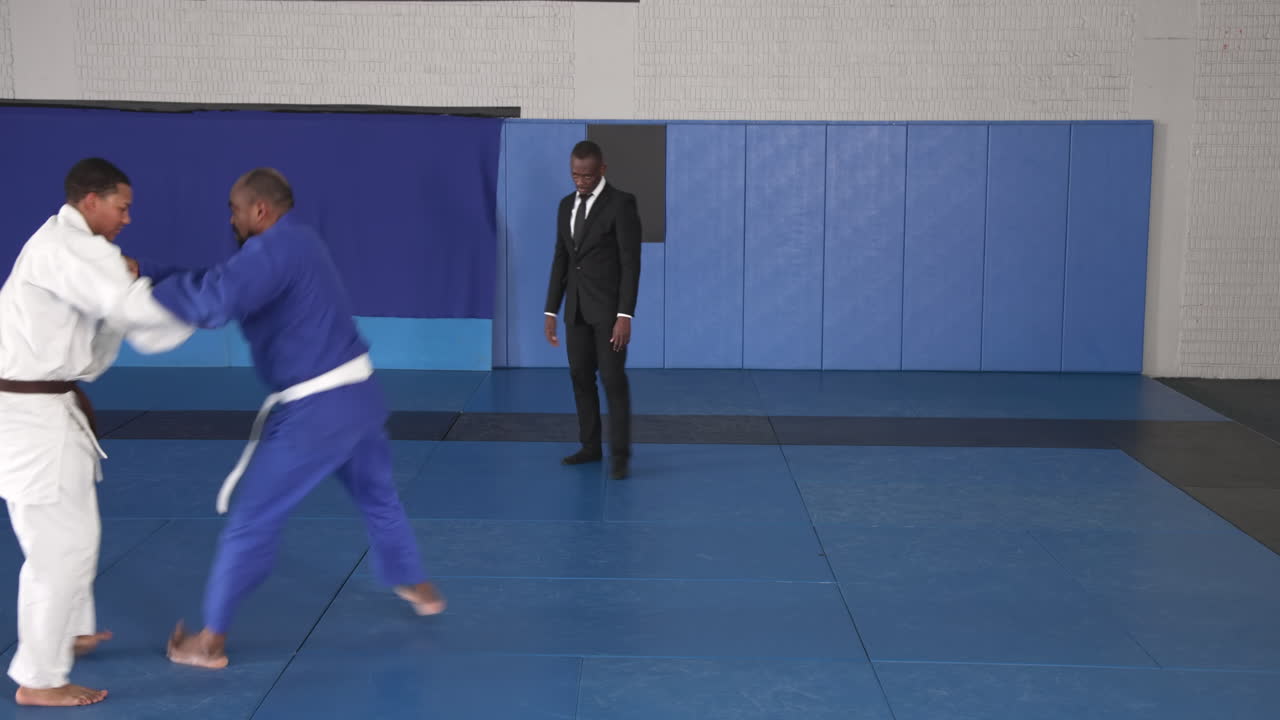 Practicing judo, athletes in action on mat with coach observing