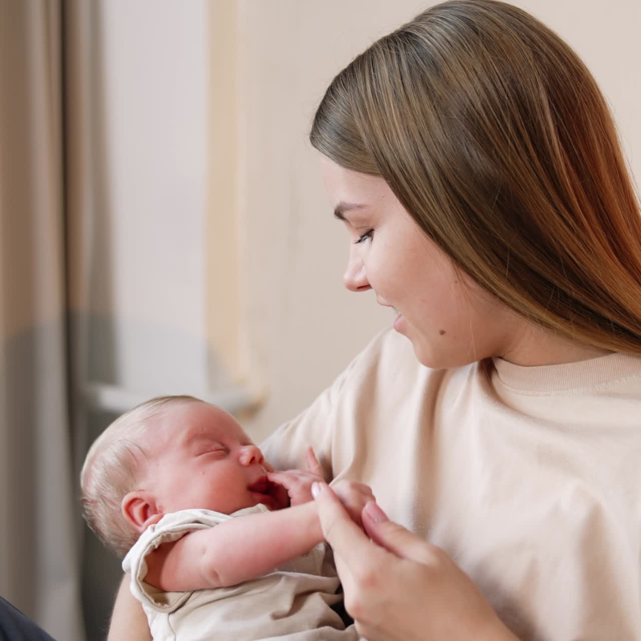 Woman with long blonde hair holding her baby. Mother takes tiny hand of a child and smiles to a kid