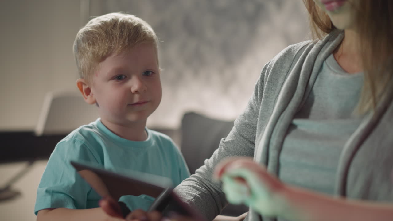 Bambino biondo paffuto guarda un cartone animato con la mamma sul tablet.