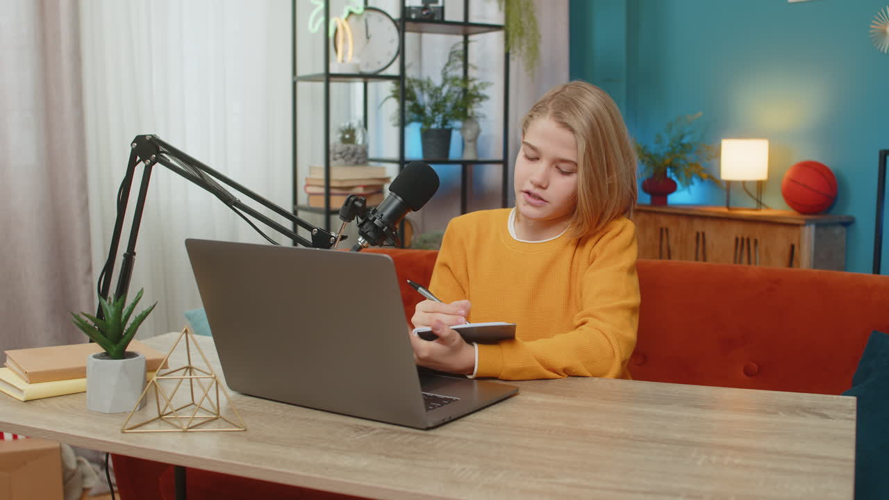 Teenager boy writing blog on laptop preparing online gaming stream with studio microphone at home