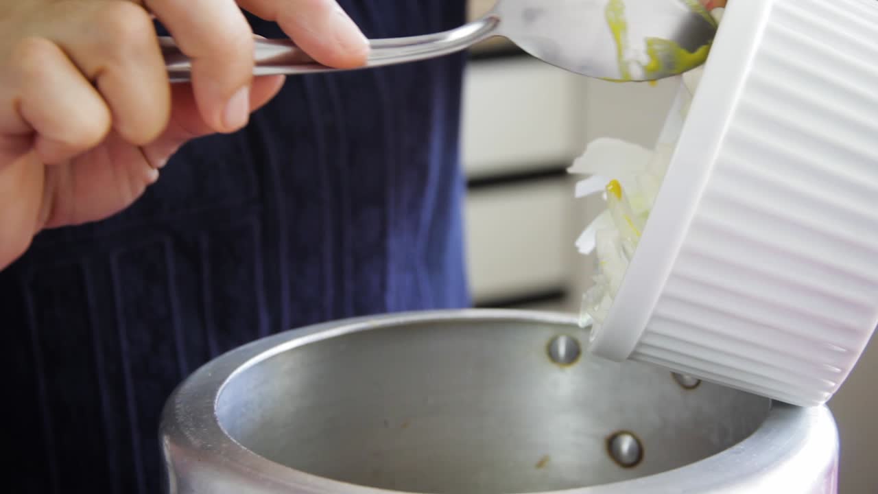 숟가락으로 압력 팬 안에 있는 흰색 그릇에서 얇게 썬 양파를 떨어뜨리는 암컷 손