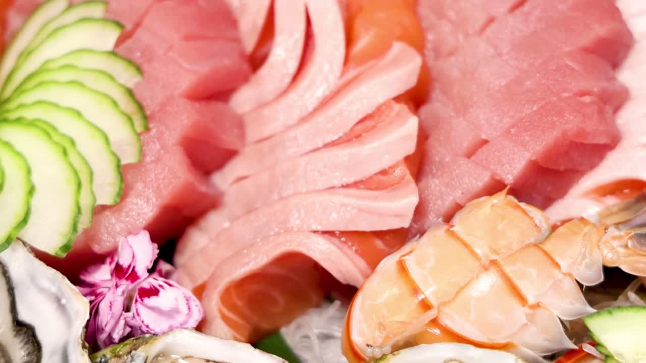 A close-up view of tuna and shrimp sashimi with cucumber and decorative flowers.