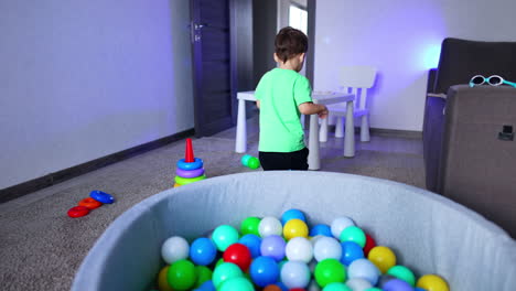 lovely caucasian toddler playing with dry pool in his room. cheerful kid throwing balls into the basin.