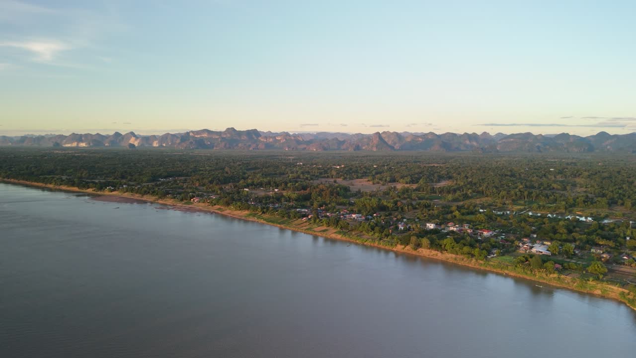 Expansive sunset drone view of the Mekong flowing past green villages with rugged mountains stretching across the skyline