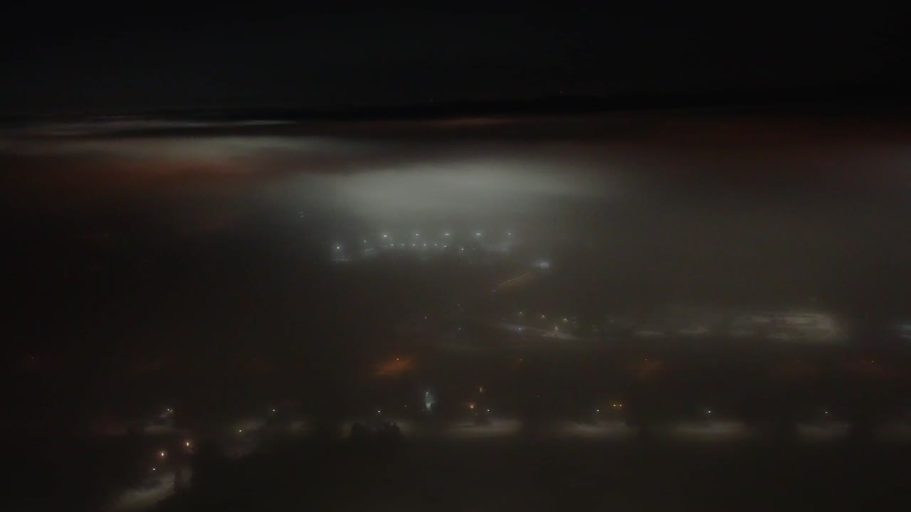 Night aerial view from above the clouds over the city of St-Constant, Québec, Canada. The city lights pierce through the cloud cover, creating a unique and atmospheric nightscape
