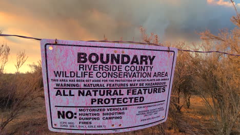 conservation boundary sign blows in wind as large wildfire burns in the background